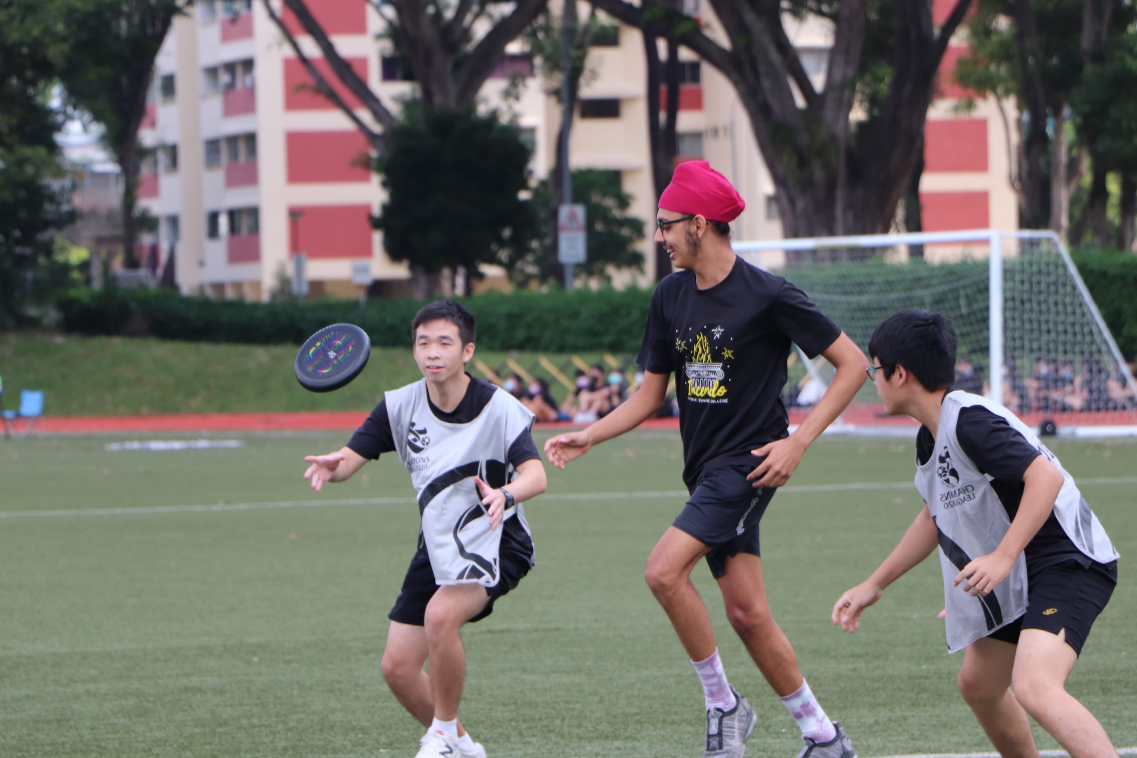 Three young men playing ultimate frisbee on a grass field, with a dark disc mid-air near the left player.